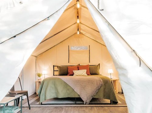 Cozy glamping tent interior featuring a bed, decorative pillows, and warm lighting.