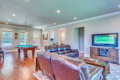 Spacious living room with leather sofas, a pool table, and a TV displaying a sports game. Bright, modern decor.