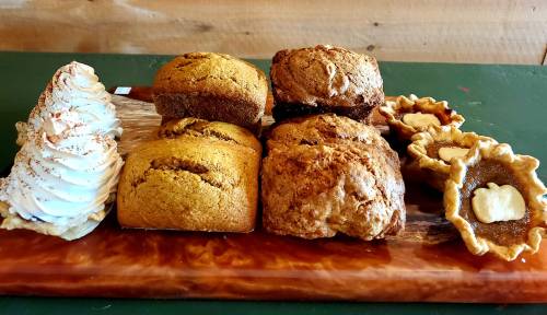 A wooden platter with assorted baked goods: loaves of bread, pastries, and mini pies.
