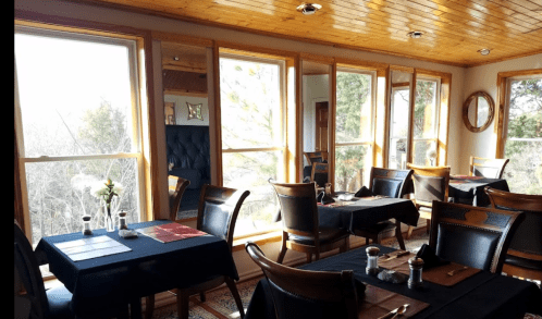 Cozy restaurant interior with wooden decor, tables set for dining, and large windows offering a view of nature.