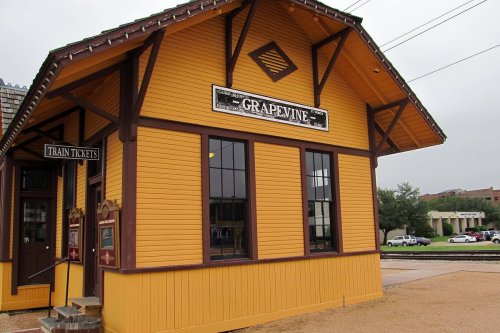 Historic yellow train station building with "Grapevine" sign, featuring large windows and a ticket booth.