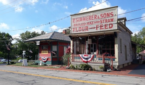 Historic storefront with "R. Shimerer & Sons" sign, featuring American flags and bunting, on a sunny day.