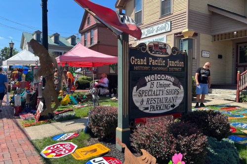 Sign for Grand Pacific Junction with colorful shops and tents in a bustling outdoor market setting.