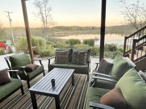 Cozy outdoor seating area with green cushions, overlooking a serene lake at sunset.