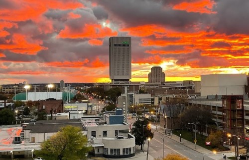 A vibrant sunset over a city skyline, with dramatic clouds and illuminated buildings.