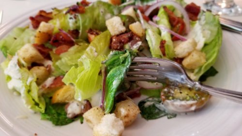 A close-up of a fresh salad with lettuce, croutons, bacon, and dressing, with a fork resting on the side.