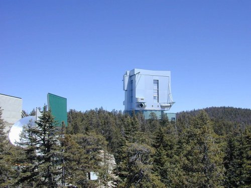 A large, modern building surrounded by trees under a clear blue sky, likely a research facility or observatory.