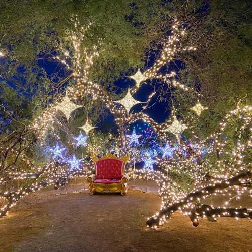 A festive scene with a red chair surrounded by twinkling lights and star-shaped decorations in a dark, enchanting setting.