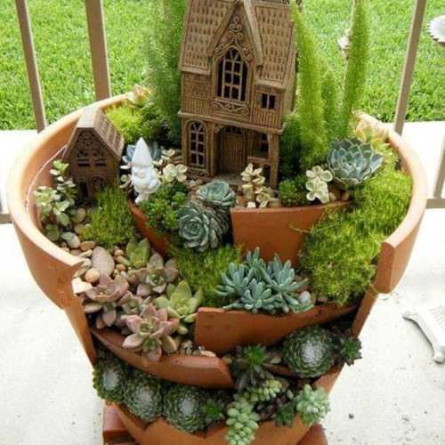 A tiered terracotta planter filled with various succulents, featuring a small house and a gnome among the greenery.