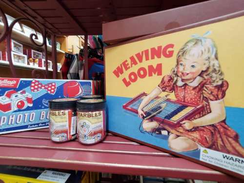 A vintage display featuring a photo book, marbles jars, and a weaving loom box with a smiling girl illustration.