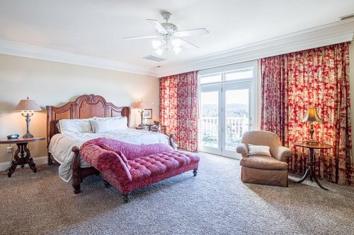 Spacious bedroom with a large bed, plush seating, and bright curtains, featuring a balcony view and soft carpet.