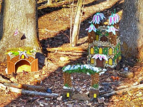 A whimsical fairy garden scene with two decorative houses made of stones and colorful flowers, set among trees.