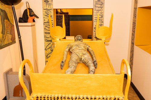 A yellow sarcophagus with a mummified figure inside, displayed in a museum setting with ancient Egyptian decor.