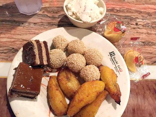 A plate with chocolate cake, sesame balls, fried plantains, and a bowl of ice cream, accompanied by fortune cookies.