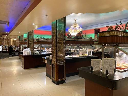 A spacious buffet restaurant with food stations, elegant decor, and a chandelier, featuring a variety of dishes.