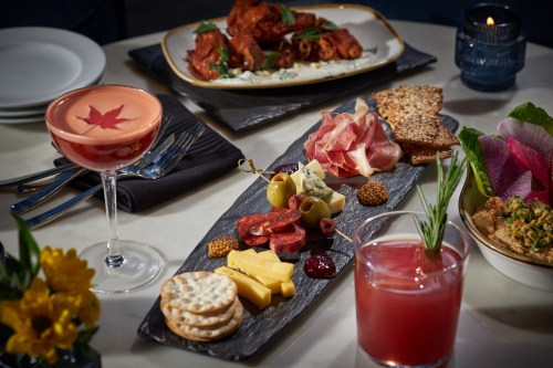 A beautifully arranged charcuterie board with meats, cheeses, olives, crackers, and cocktails on a dining table.