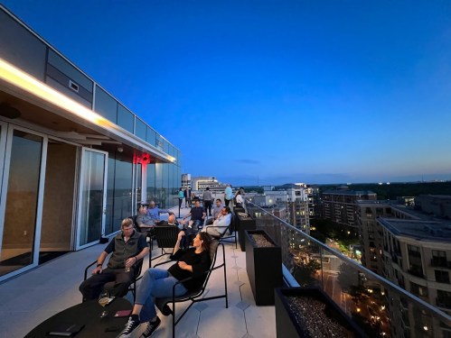 A rooftop gathering at dusk, with people seated and enjoying the view of the city skyline.