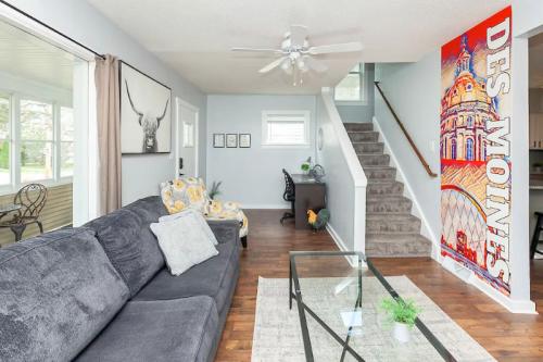 Cozy living room with a gray sofa, glass coffee table, and colorful wall art, leading to a staircase. Bright and inviting space.