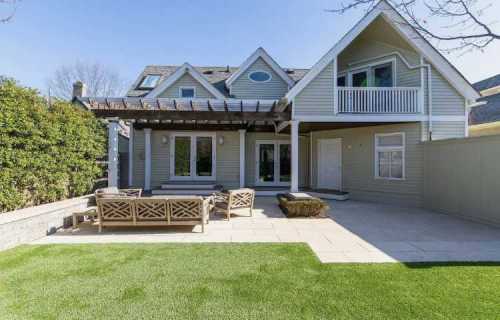A modern house with a patio, outdoor seating, and a well-maintained lawn under a clear blue sky.