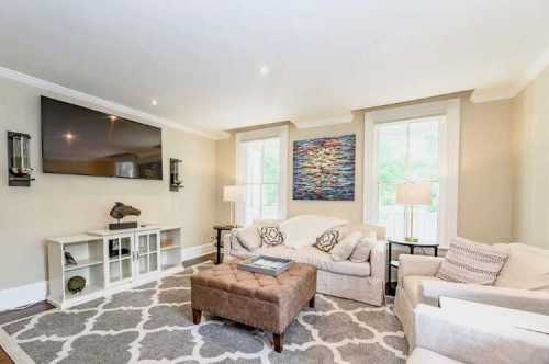 Cozy living room with a large TV, light-colored sofas, a decorative rug, and a colorful wall art piece.