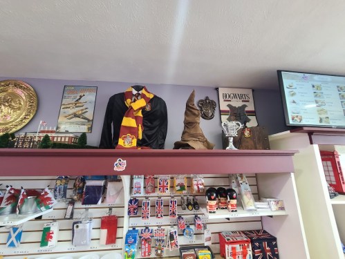 Display of Harry Potter merchandise, including a robe, scarf, Sorting Hat, and various souvenirs on shelves.