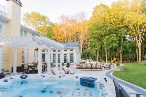 A backyard with a hot tub, patio furniture, and trees with autumn foliage in the background.
