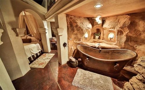 Cozy bathroom with a copper bathtub, stone walls, and soft lighting, creating a warm, rustic atmosphere.