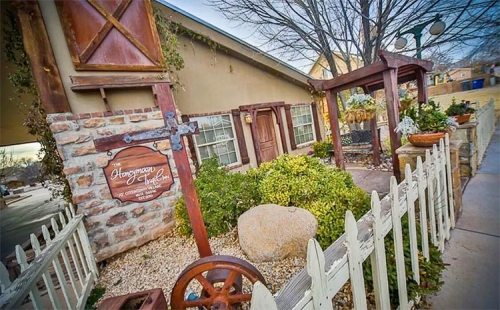 Charming stone building with a wooden sign, surrounded by greenery and a white picket fence.