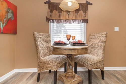 Cozy dining nook with a round table, two woven chairs, and decorative plates, set against a warm, earthy backdrop.