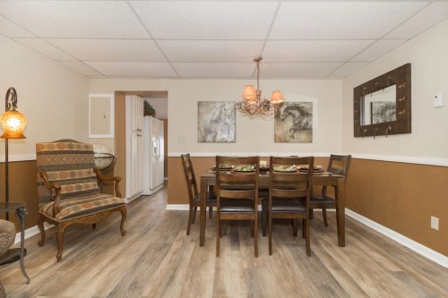 A cozy dining area with a wooden table, chairs, and artwork on the walls, featuring warm lighting and a patterned chair.