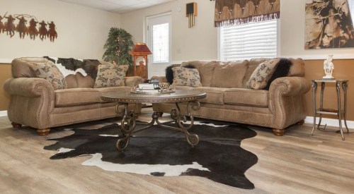 Cozy living room with a brown sofa, decorative pillows, a round coffee table, and a cowhide rug on wooden flooring.