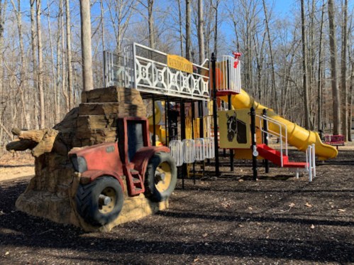 A colorful playground with a tractor-themed structure and a yellow slide, surrounded by bare trees in a park.