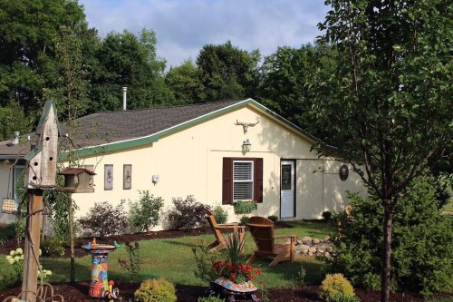 A charming yellow house surrounded by greenery and garden decor, featuring a cozy outdoor seating area.