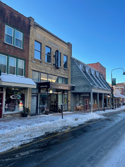 A snowy street scene featuring historic buildings, including the Hudson Hotel, under a clear blue sky.