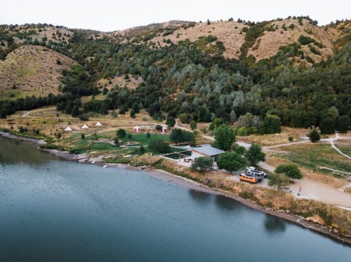 Aerial view of a lakeside campsite with tents, trees, and hills in the background.
