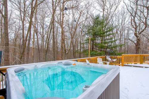 A hot tub on a snowy deck surrounded by bare trees, creating a serene winter landscape.