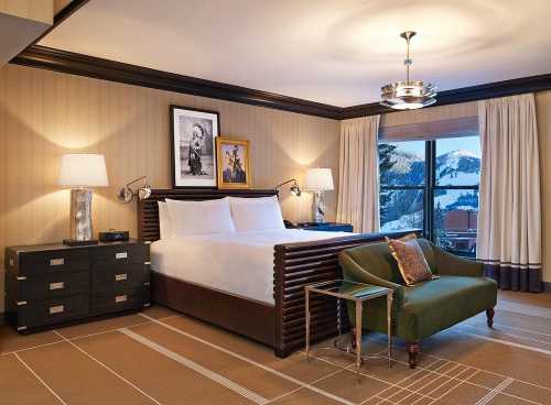 A stylish hotel room featuring a king bed, green armchair, nightstands, and a scenic mountain view through the window.