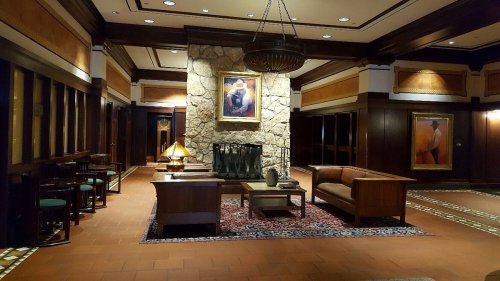 Cozy hotel lobby featuring a stone fireplace, wooden accents, seating area, and artwork on the walls.