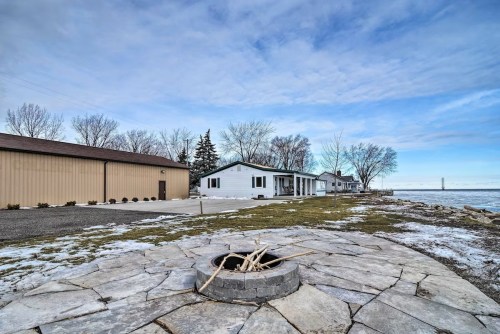A lakeside property with a fire pit, grassy area, and houses under a cloudy sky.