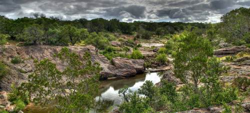 A serene landscape featuring a rocky riverbed surrounded by lush greenery and overcast skies.