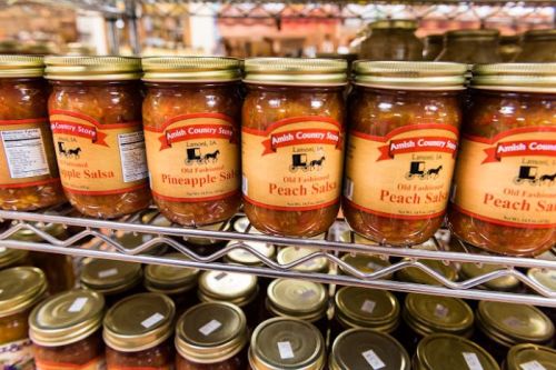 Jars of pineapple and peach salsa on a shelf, labeled with "Amish Country Store" in a rustic setting.