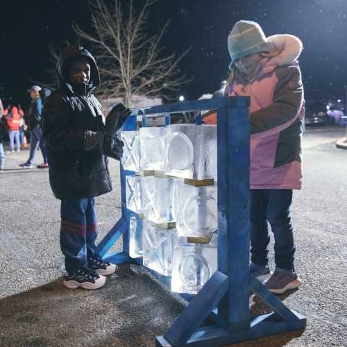 Two children interact with a display of ice blocks at a nighttime event, surrounded by a festive atmosphere.