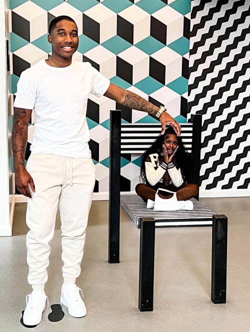 A man stands beside a large striped chair, while a girl sits playfully on the seat, smiling at the camera.