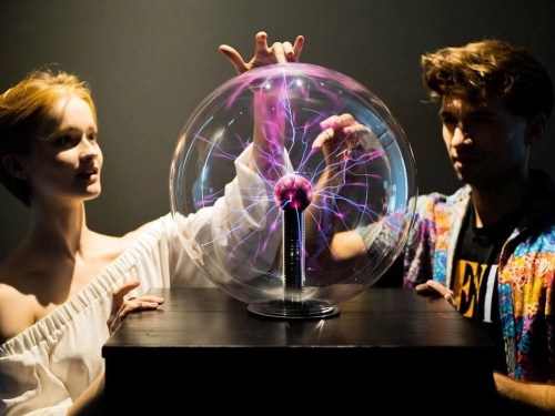 A woman and a man interact with a plasma globe, creating electric arcs inside a glass sphere.