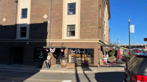 A brick building with a café entrance, outdoor seating, and patriotic decorations on a sunny day.