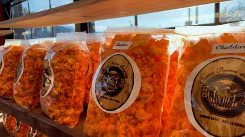 Bags of cheddar popcorn lined up on a shelf, with bright orange kernels visible through clear packaging.