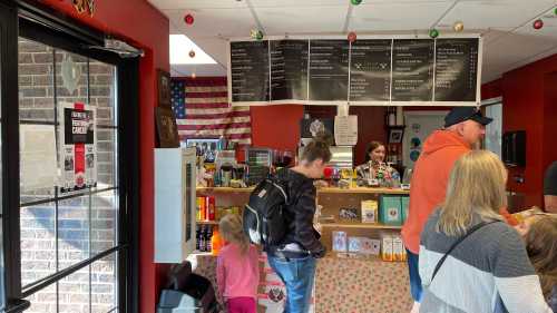 A busy shop interior with a counter, customers browsing, and an American flag on the wall. Colorful products displayed.