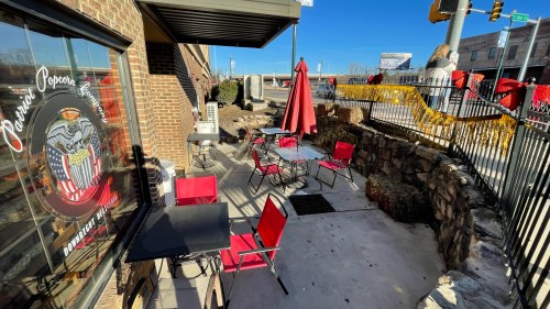 Outdoor seating area of a café with red chairs and tables, featuring a sunny day and a decorative fence.