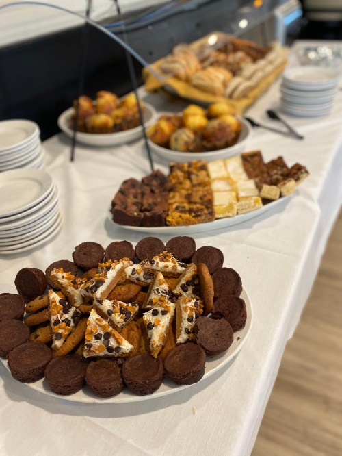 A table spread with various baked goods, including cookies, brownies, and pastries, on white tablecloth.