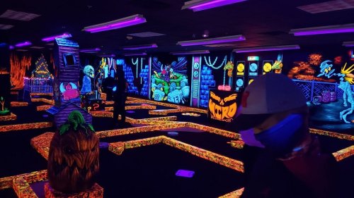 A vibrant glow-in-the-dark mini-golf course with colorful decorations and neon lights.